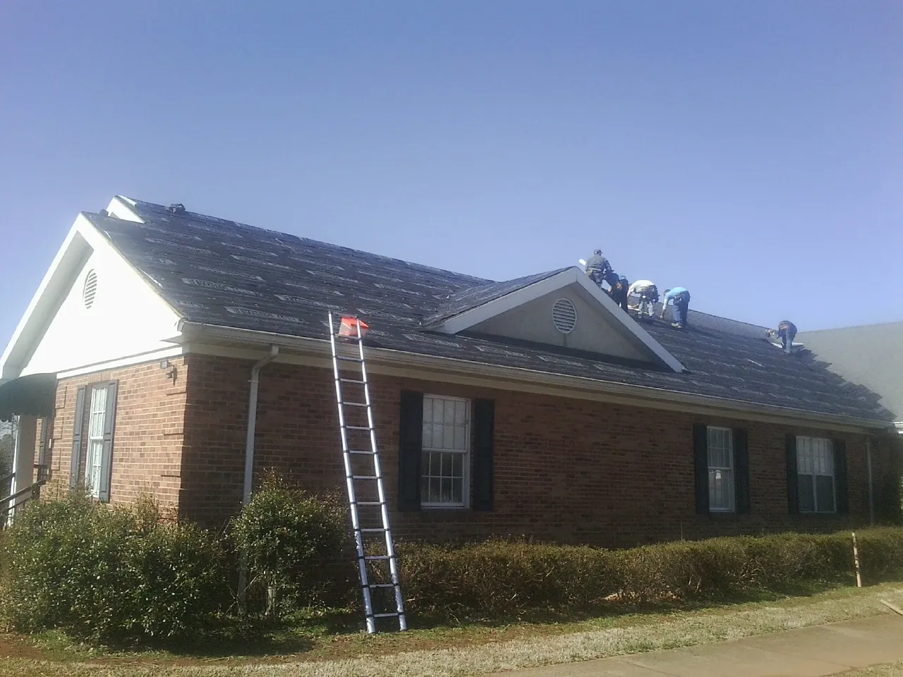 Crew tearing shingles off a brick ranch roof with a ladder set — Metal Roof Repair work by our crew in Indian Head