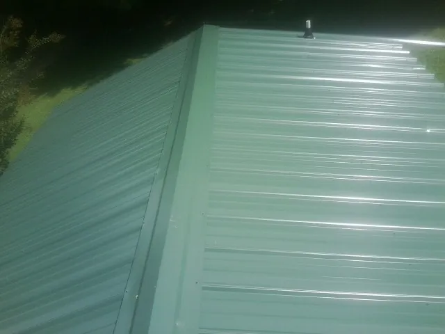 New green metal panels meeting at the ridge of a roof — Flat Roof Repair work by our crew in Indian Head