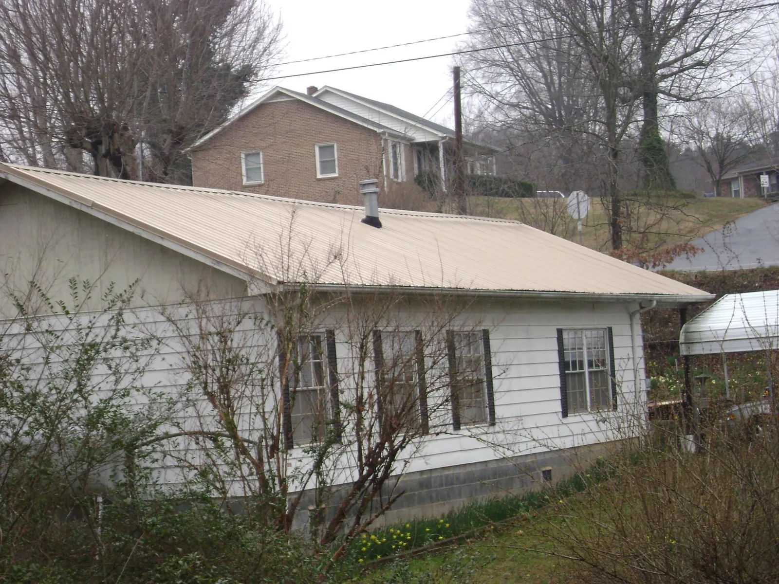Tan metal roof on a white sided house set into a hillside — Commercial Roofing by Roofing Brothers in Indian Head